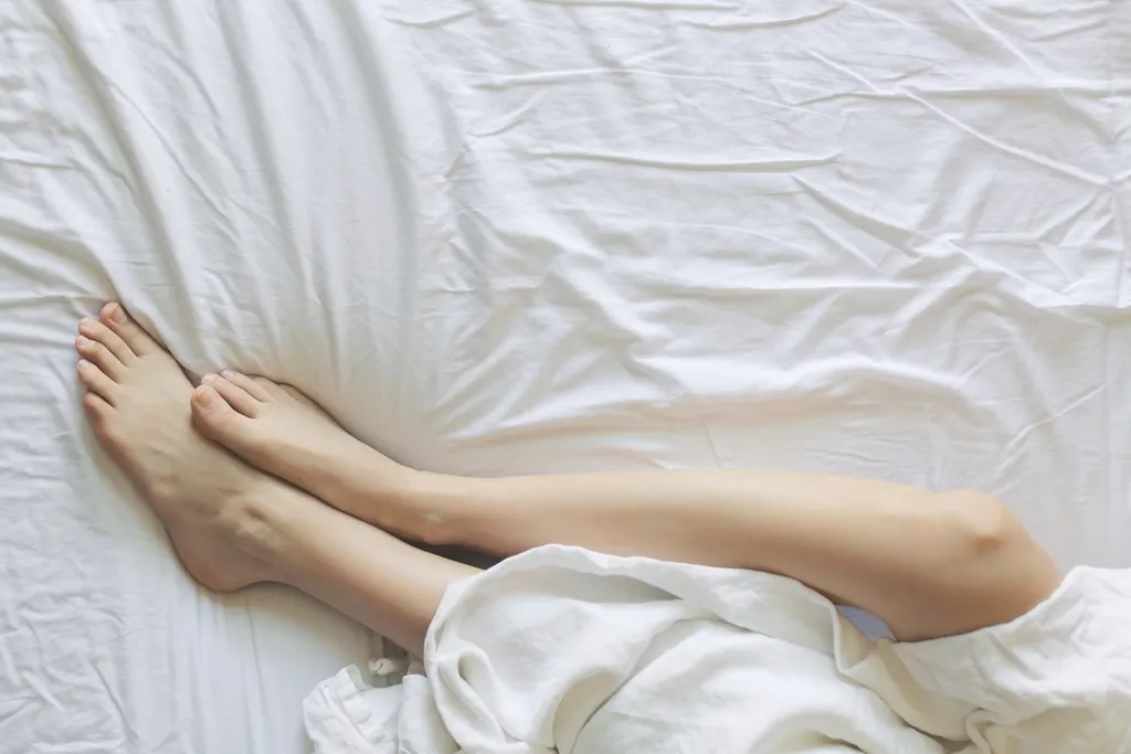 Piernas sobre una cama con sábanas blancas