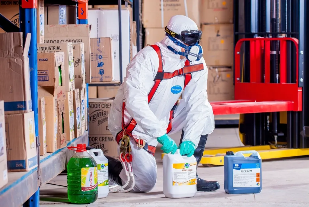 Trabajador con mono y equipo de protección junto a productos químicos
