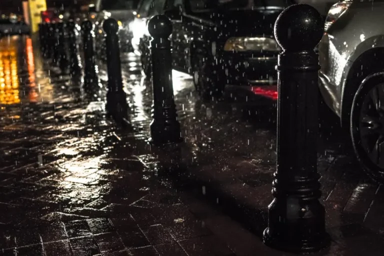Acera mojada de una calle de ciudad por la noche, con bolardos