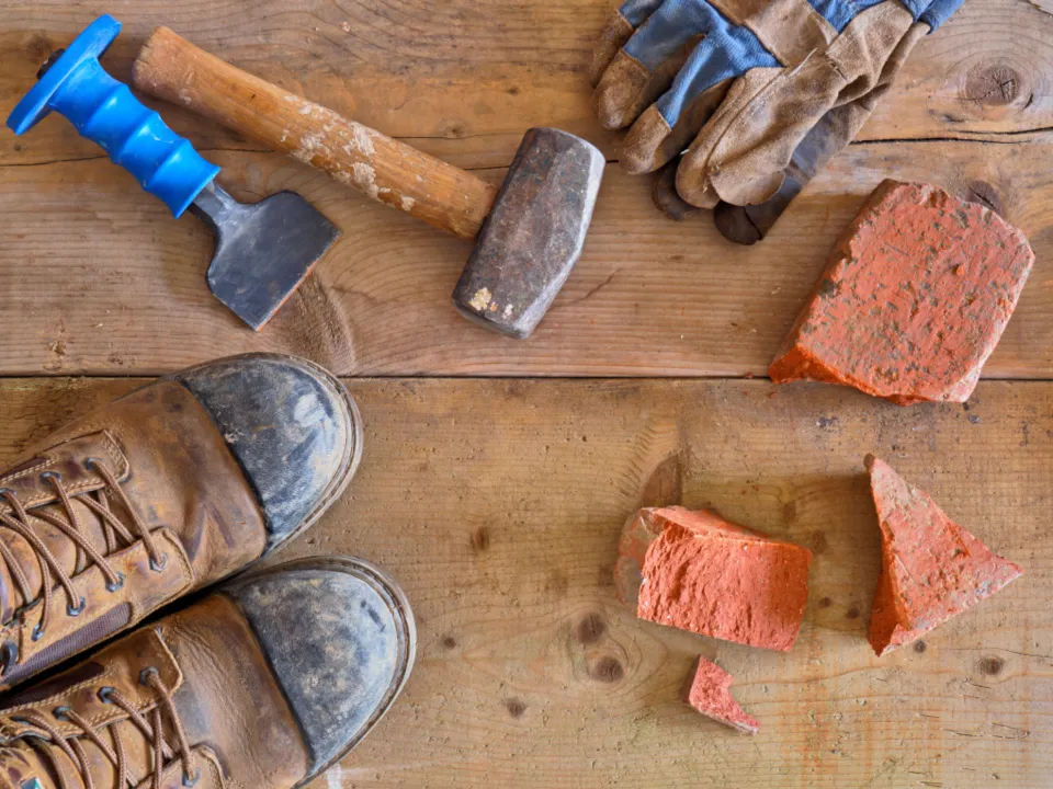 Botas de trabajo, guantes y herramientas sobre una mesa de madera