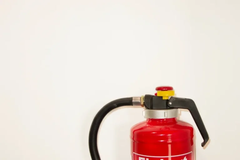 Extintor rojo junto a una pared blanca